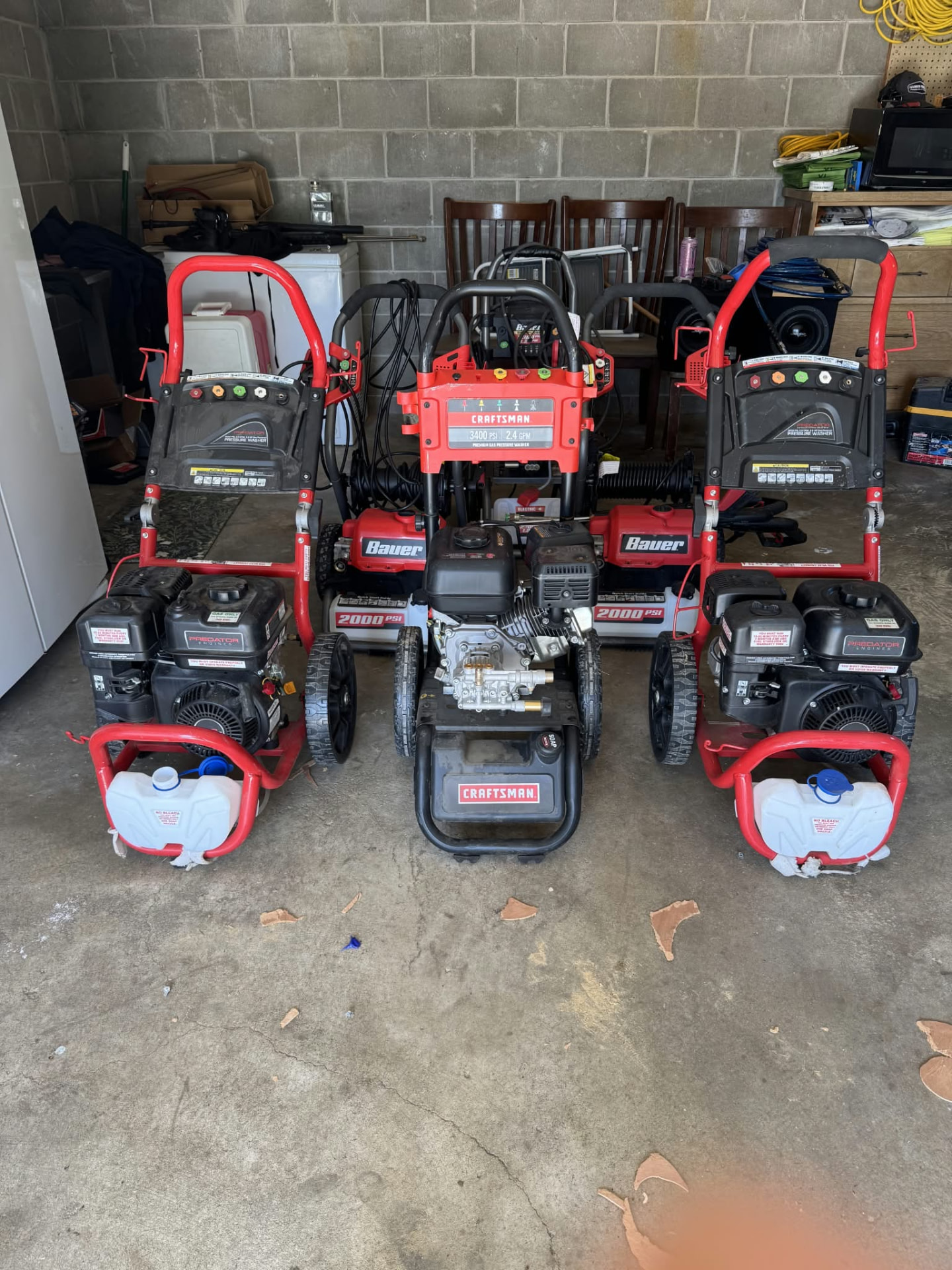 Three gas pressure washers lined up inside a garage, ready for a power washing job